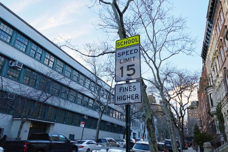 a speed limit sign for 15 mph across the street from a school on a nyc street